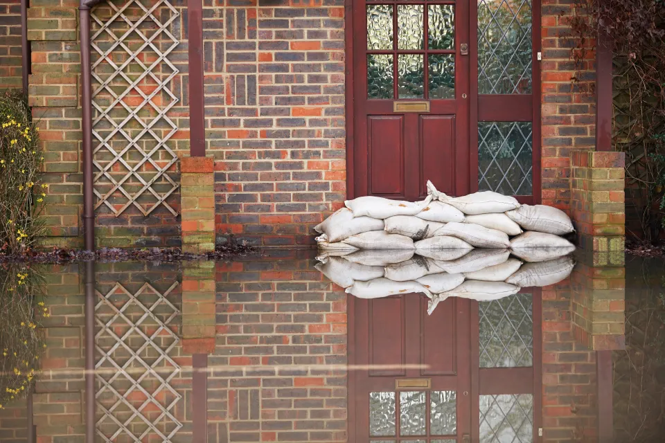 Sandbags stacked in front of a red door on a brick building with ground in front flooded with water